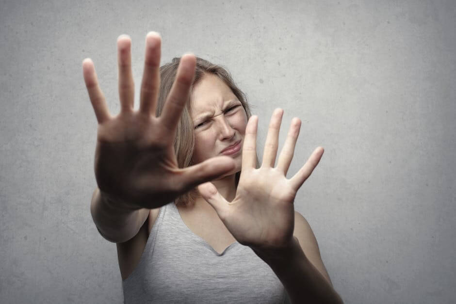 Woman with fearful expression, hands raised in self-defense. Healing PTSD.