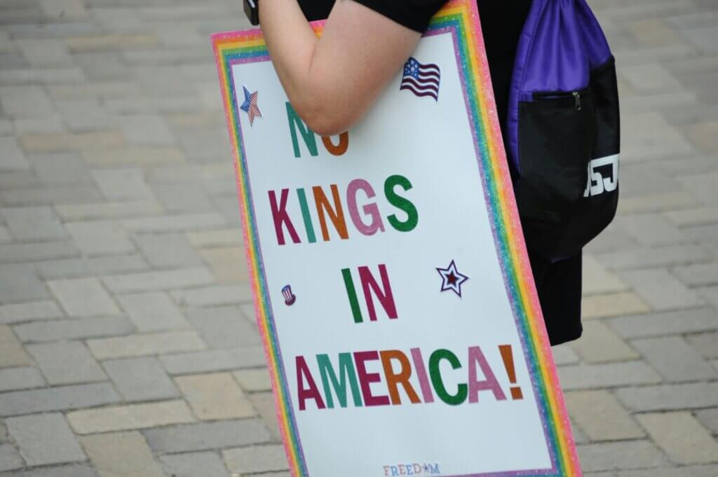 Person holding a sign that says "No Kings in America! Compassion in Adversity
