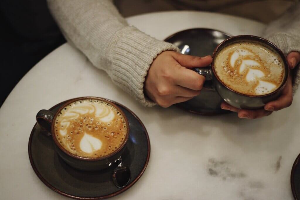 Two lattes on a café table, one held in sweater-covered hands – finding comfort when the Cornell 7 news is triggering